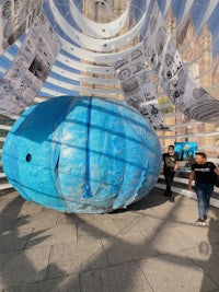a large blue ball in a building with people walking around it